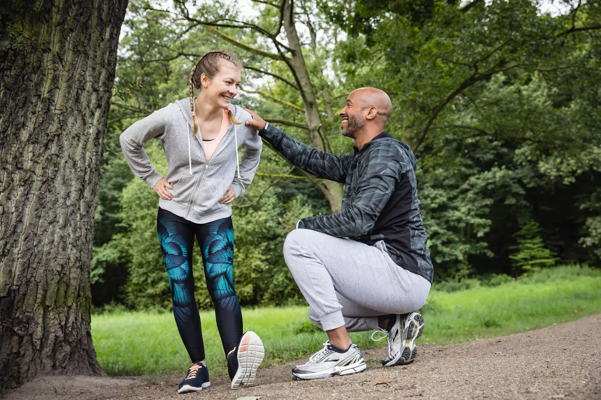 Frau macht Dehnungsübungen vor dem Laufen, Personal Trainer in der Hocke vor ihr gibt Ratschläge. Frau macht Dehnungsübungen vor dem Laufen, Personal Trainer in der Hocke vor ihr gibt Ratschläge.