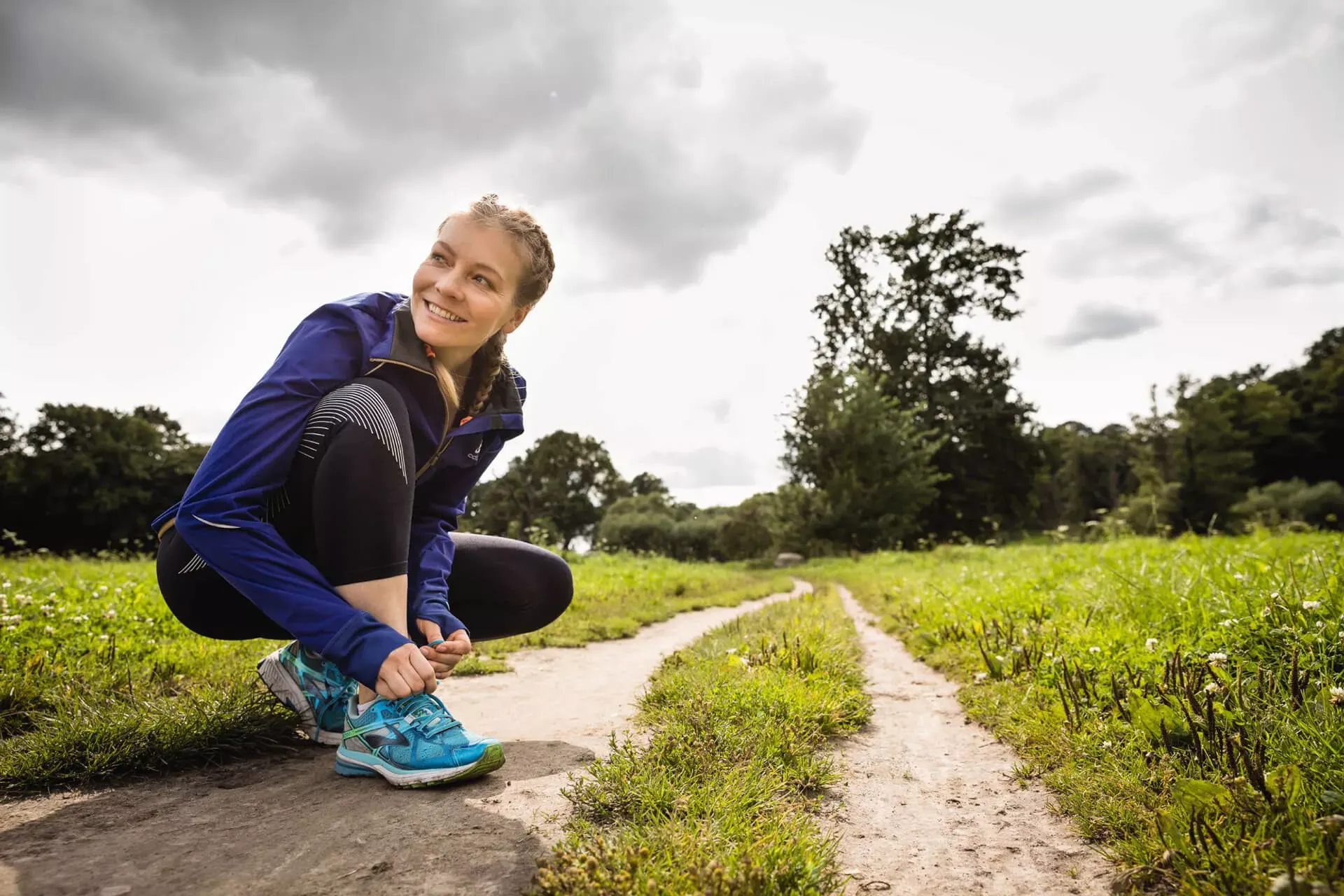 Junge Frau schnürt Laufschuh auf einem Feldweg. Junge Frau schnürt Laufschuh auf einem Feldweg.