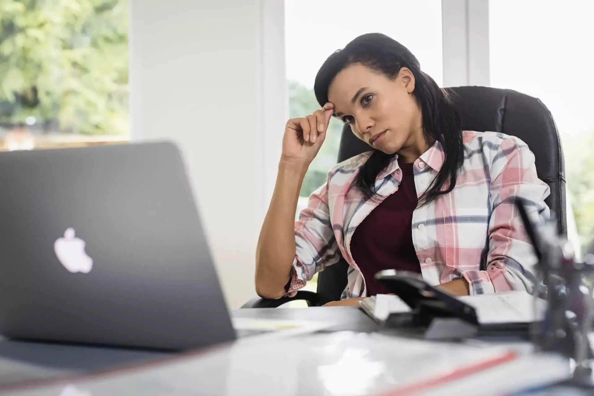 Junge Frau sitzt im Homeoffice vor ihrem Laptop und fasst sich müde an die Stirn. Junge Frau sitzt im Homeoffice vor ihrem Laptop und fasst sich müde an die Stirn.