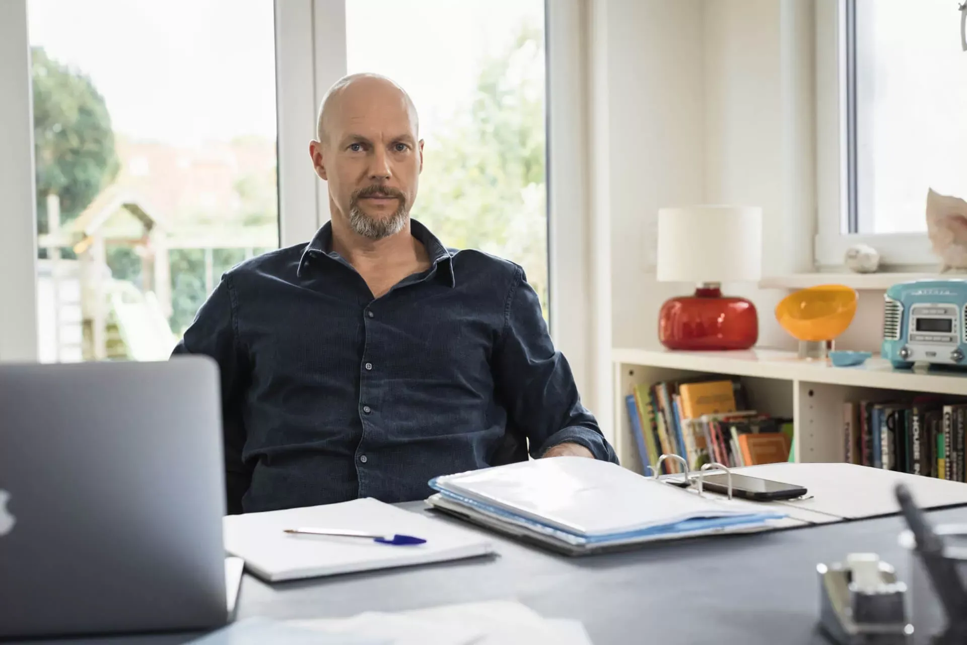 Mann sitzt im Homeoffice am Schreibtisch und schaut in die Kamera. Mann sitzt im Homeoffice am Schreibtisch und schaut in die Kamera.
