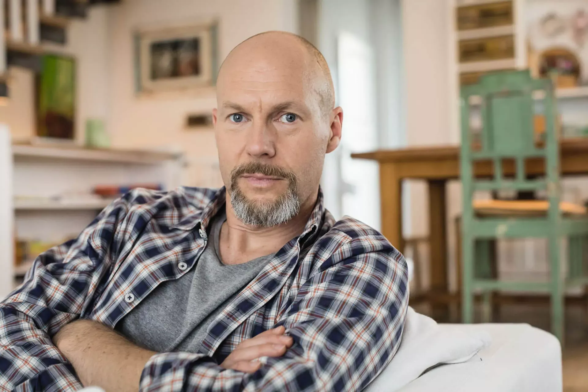 Mann im mittleren Alter sitzt auf dem Sofa mit verschränkten Armen und schaut nachdenklich. Mann im mittleren Alter sitzt auf dem Sofa mit verschränkten Armen und schaut nachdenklich.