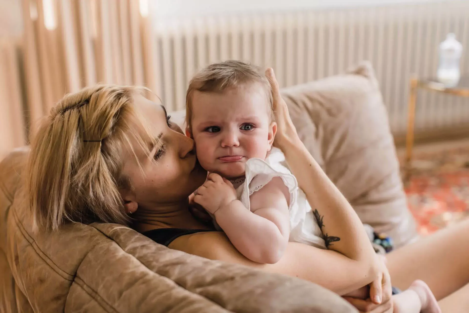 Junge Mutter sitzt mit weinendem Baby auf dem Sofa. Junge Mutter sitzt mit weinendem Baby auf dem Sofa.