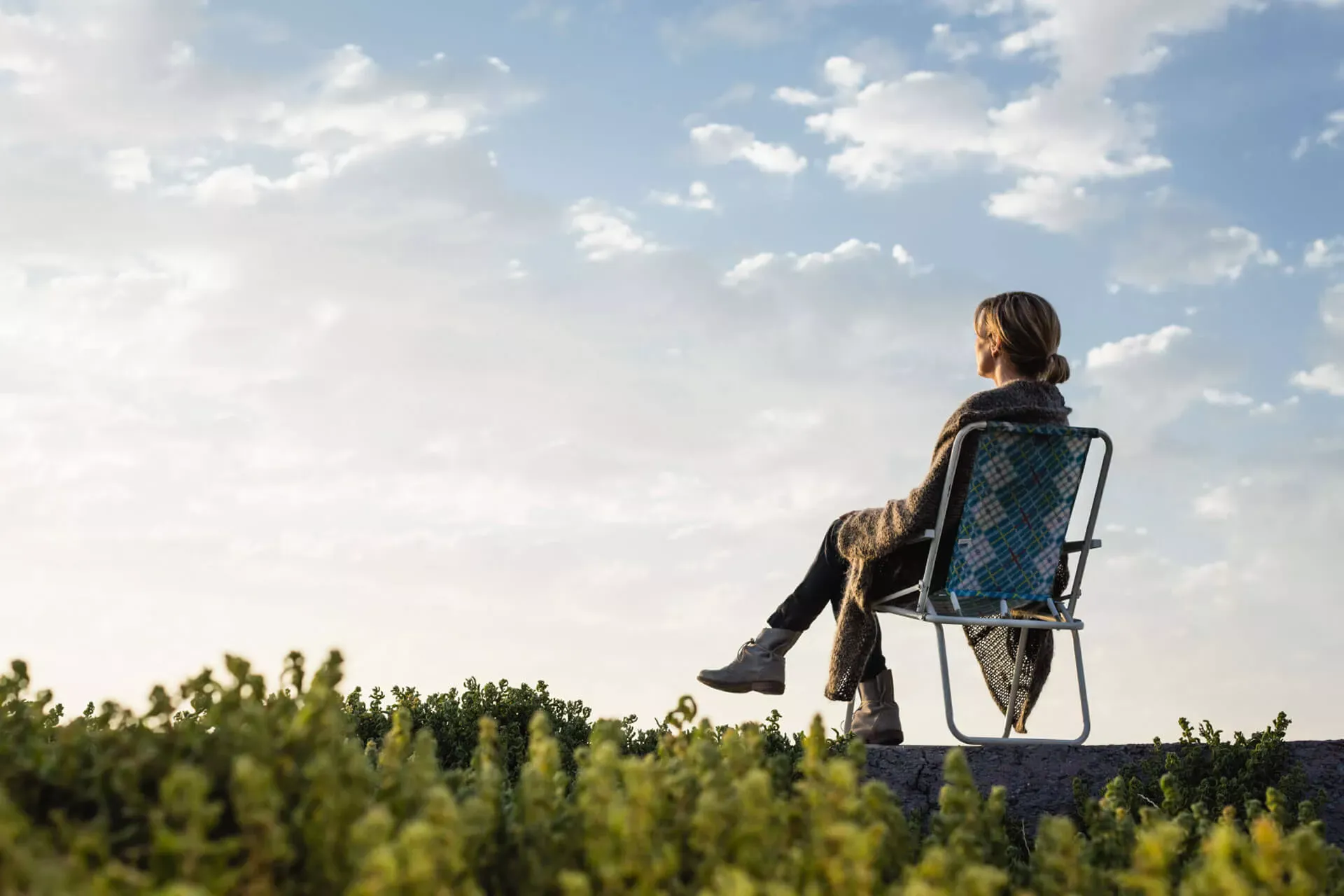 Frau sitzt auf einem Klappstuhl in der Natur und schaut in den Abendhimmel. Frau sitzt auf einem Klappstuhl in der Natur und schaut in den Abendhimmel.