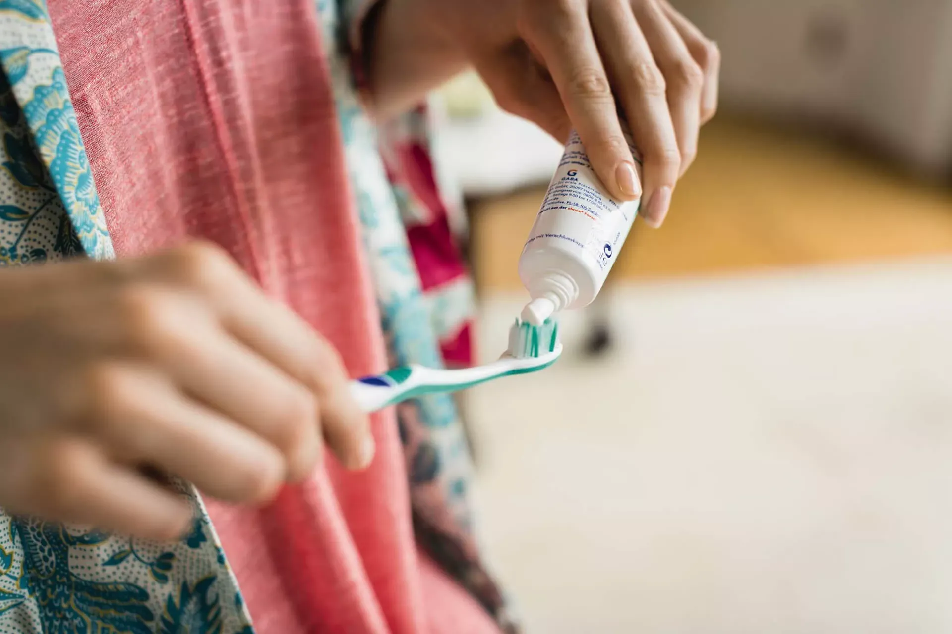 Frau in buntem Bademantel drückt Zahncreme aus einer Tube auf eine Handzahnbürste. Frau in buntem Bademantel drückt Zahncreme aus einer Tube auf eine Handzahnbürste.