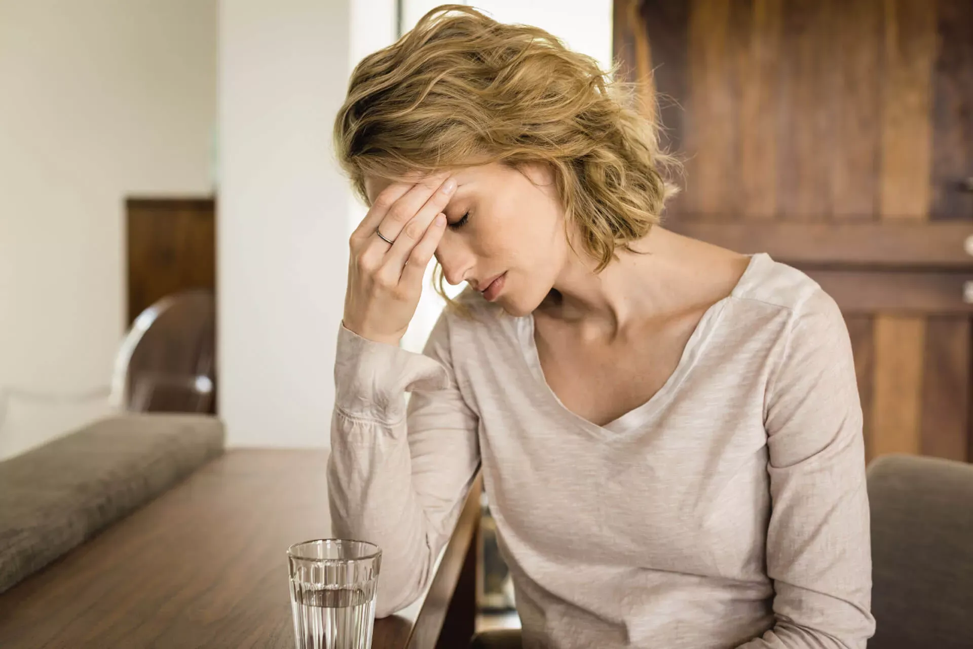 Junge Frau hält sich den schmerzenden Kopf, vor sich ein Glas Wasser. Junge Frau hält sich den schmerzenden Kopf, vor sich ein Glas Wasser.