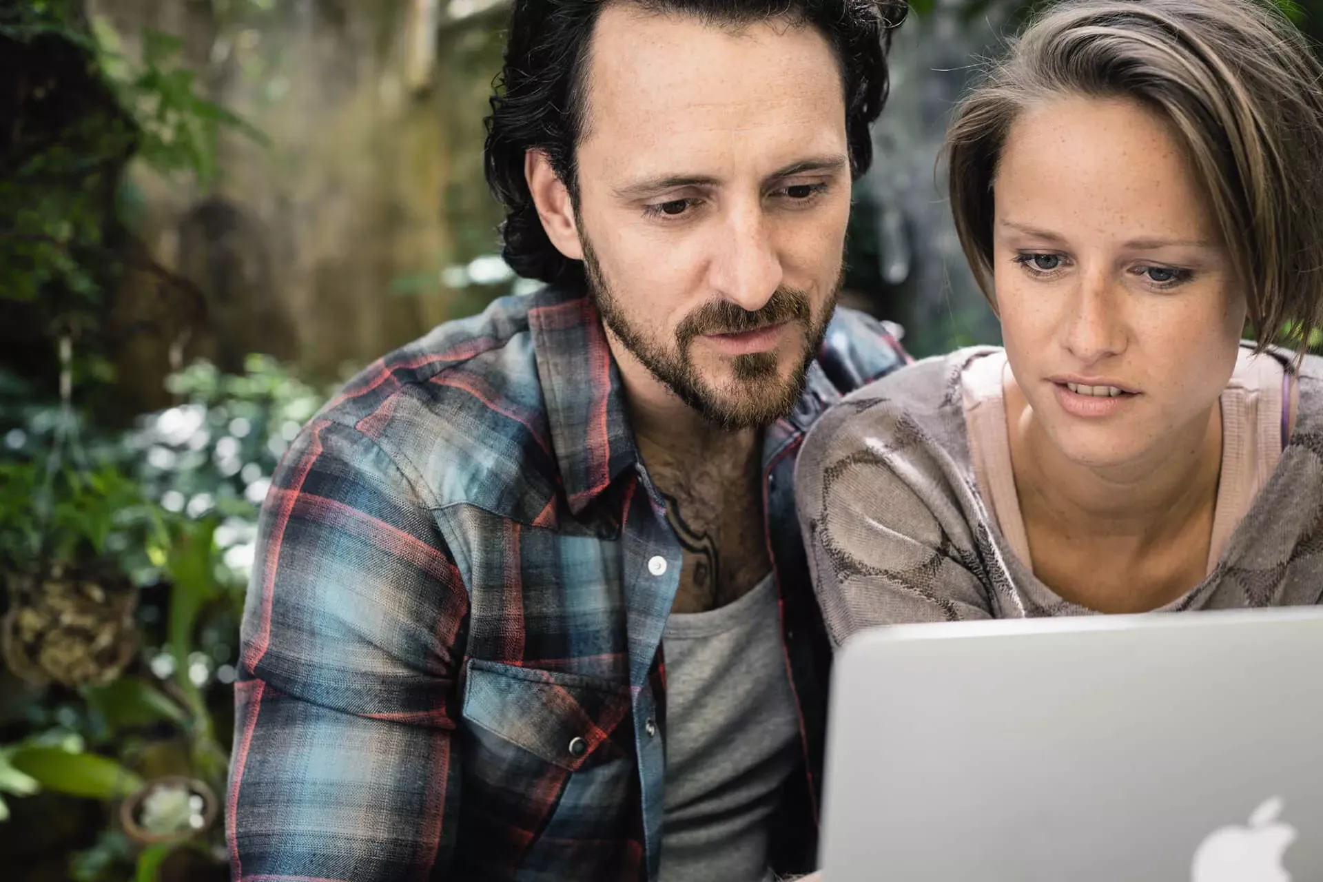 Junges Paar sitzt im Garten und schaut zusammen auf einen Laptop-Bildschirm. Junges Paar sitzt im Garten und schaut zusammen auf einen Laptop-Bildschirm.
