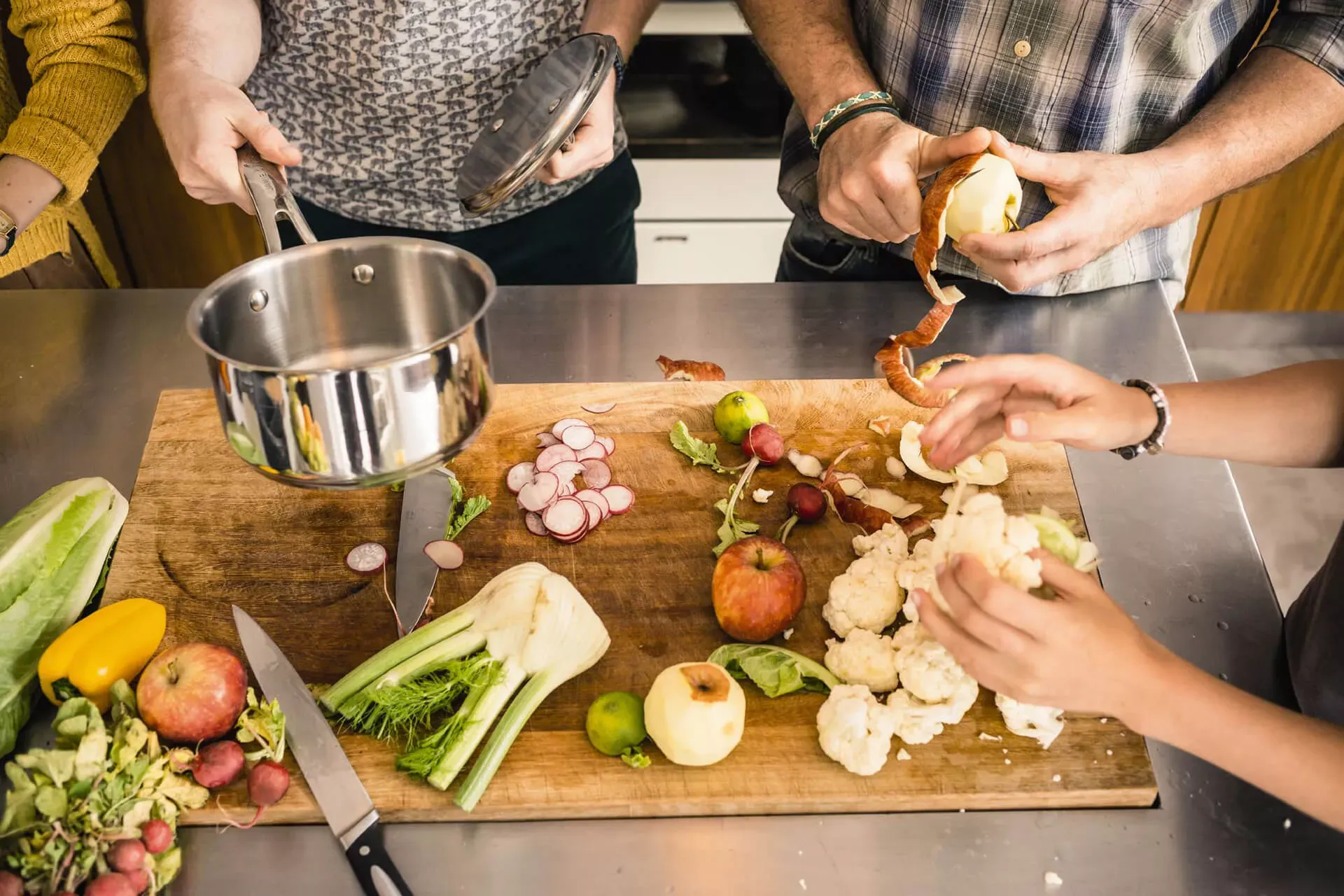 Mehrere Personen kochen arbeiten in der Küche an einem Holzbrett mit Gemüse und Obst. Mehrere Personen kochen arbeiten in der Küche an einem Holzbrett mit Gemüse und Obst.