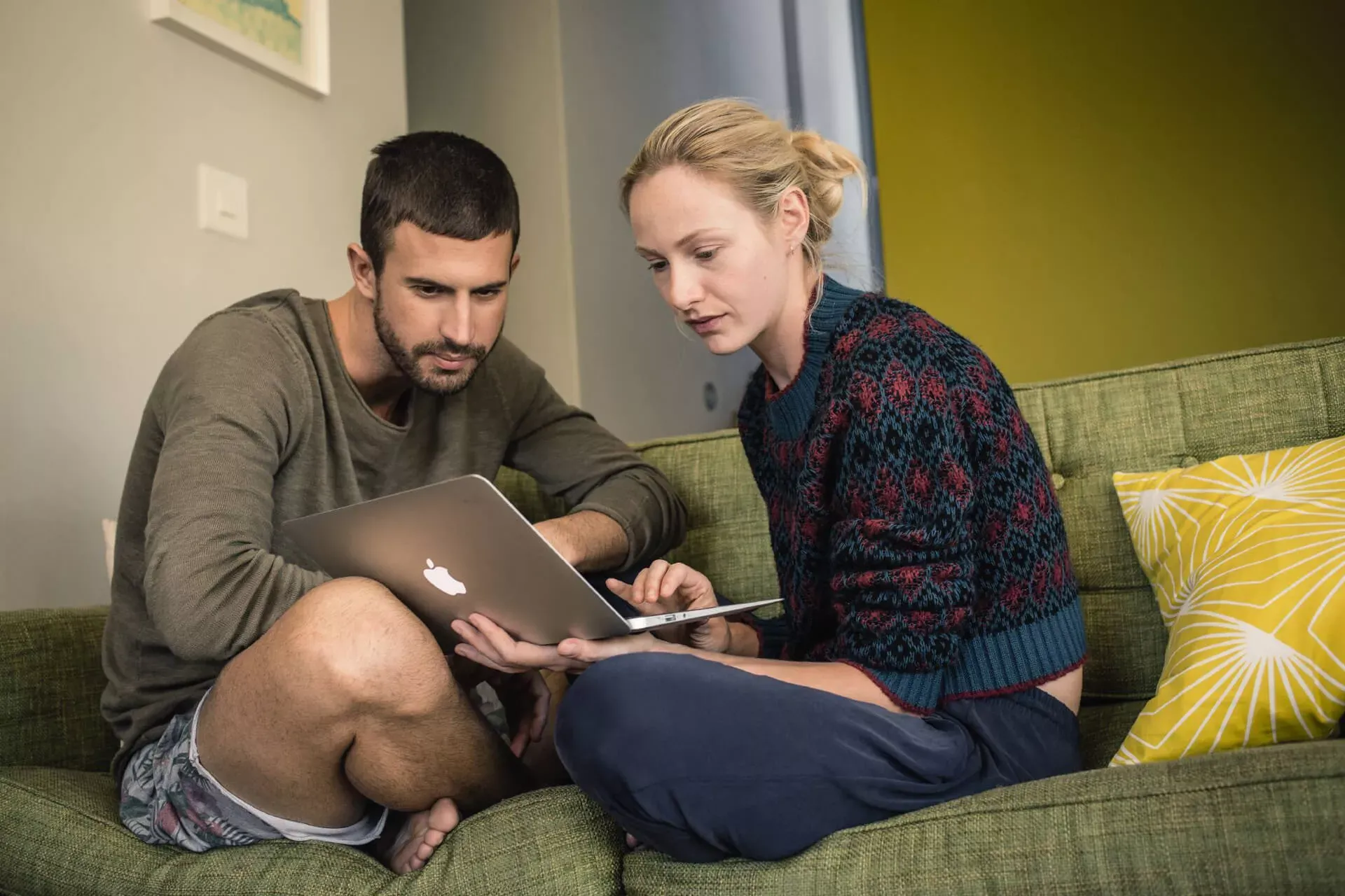 Junges Paar sitzt im Schneidersitz auf dem Sofa und schaut zusammen in ein Notebook. Junges Paar sitzt im Schneidersitz auf dem Sofa und schaut zusammen in ein Notebook.